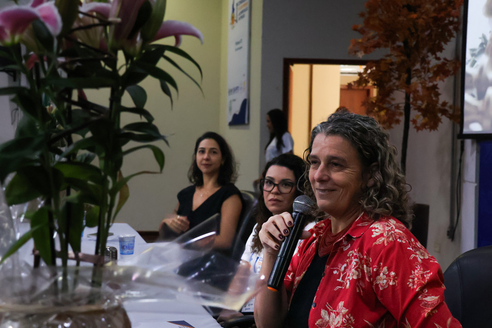 mulheres estão sentadas diante de uma mesa com microfone na mão